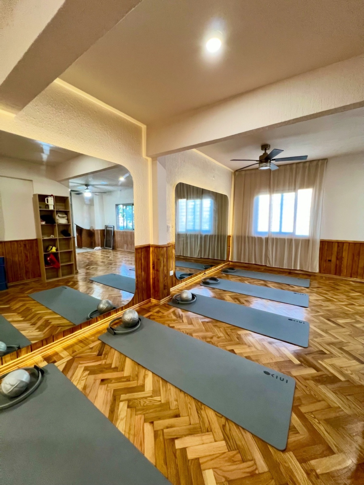 La sala del estudio: piso de parquet en espiga, tapetes de Pilates alineados y ventanas con luz natural.